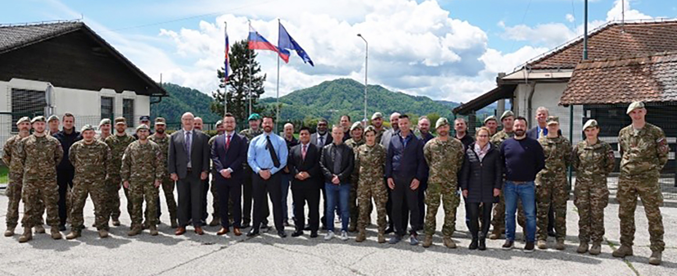 A large group of people pose for a photo outside. Slovenian flags fly behind them.