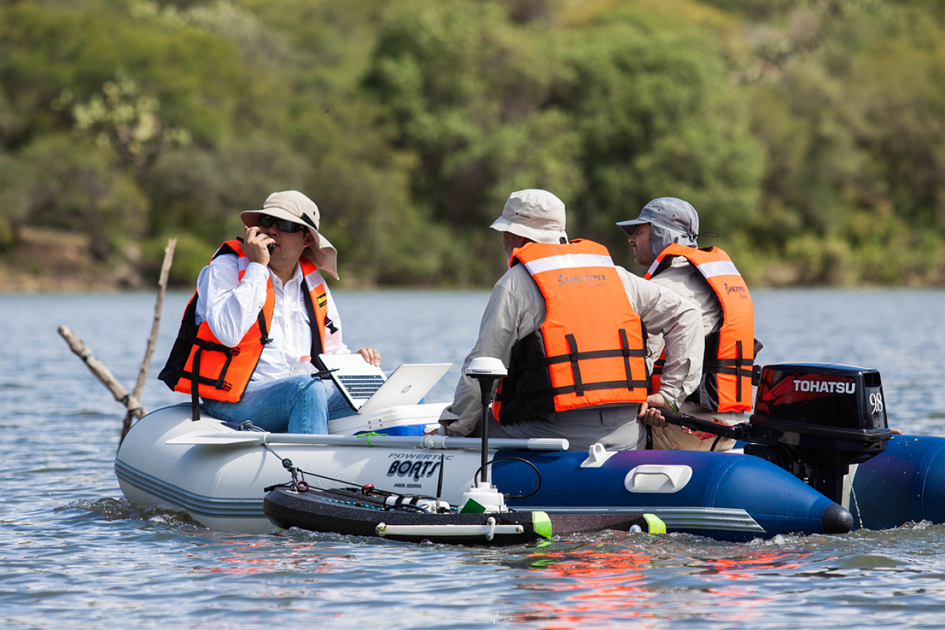 Three people wearing life jackets sit in a small, inflatable boat.