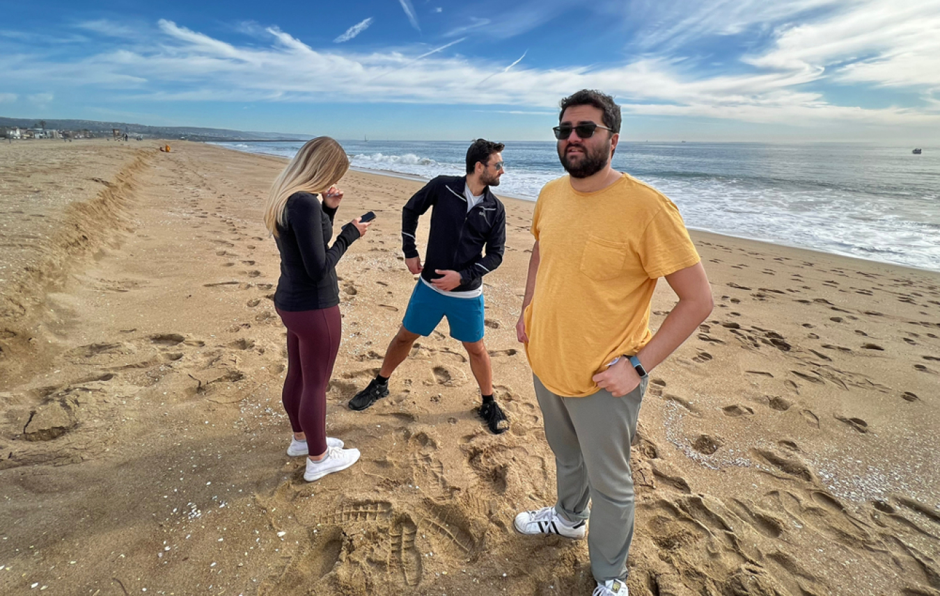 Three people stand on a beach with the ocean in the background.