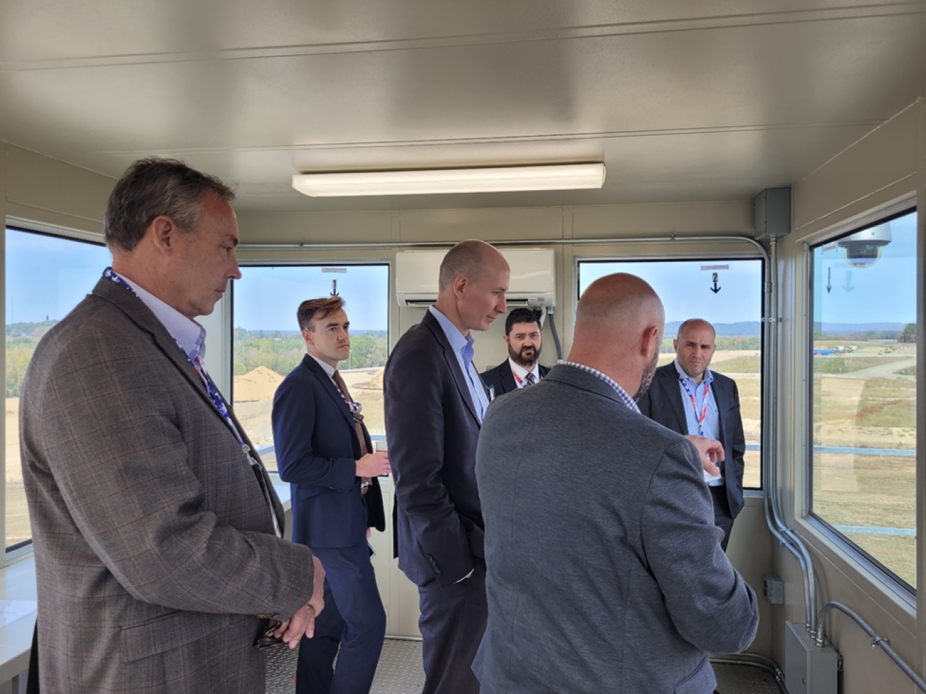 A group of men in suits listen to a speaker