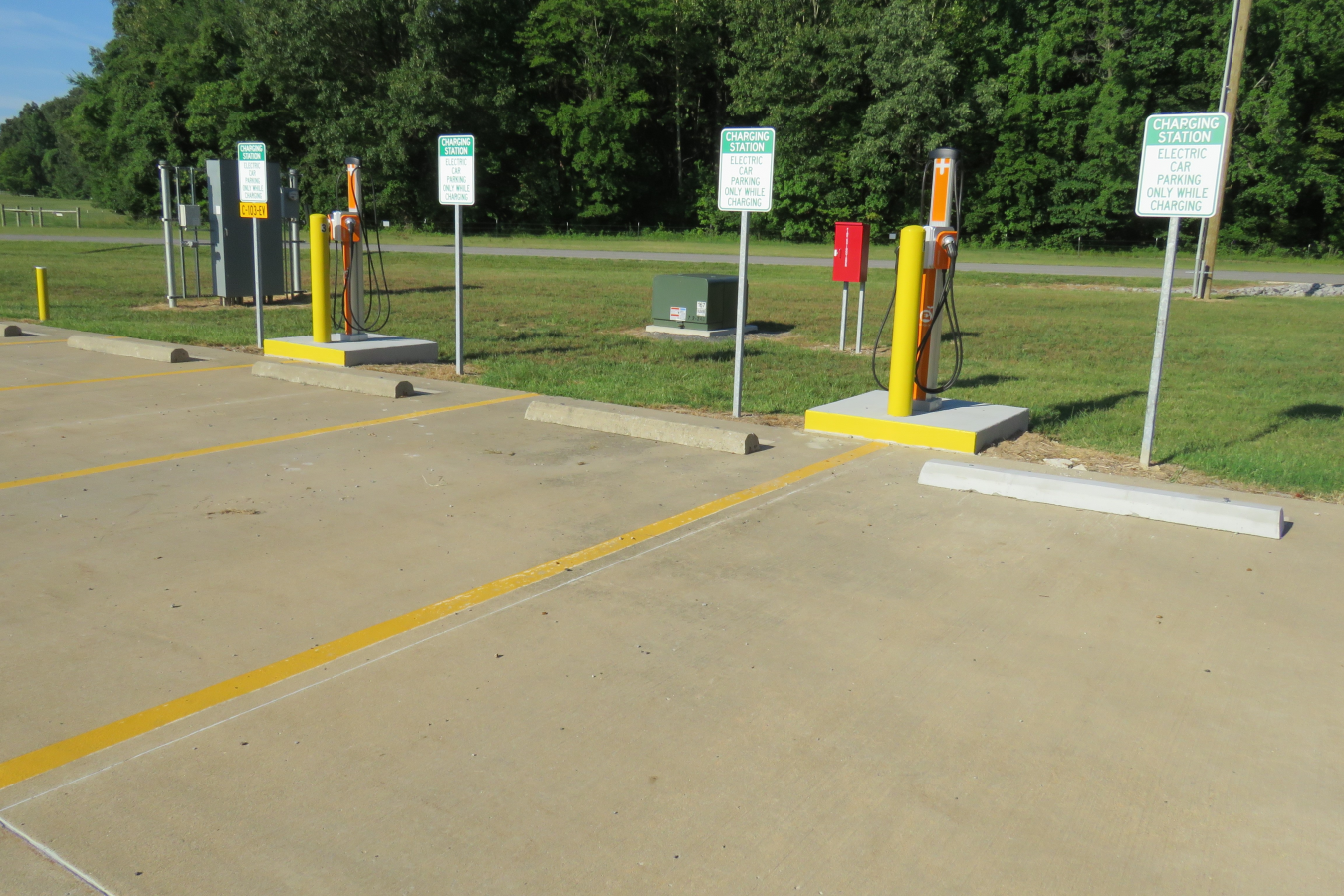 Two yellow and orange electric vehicle chargers at the edge of a parking lot