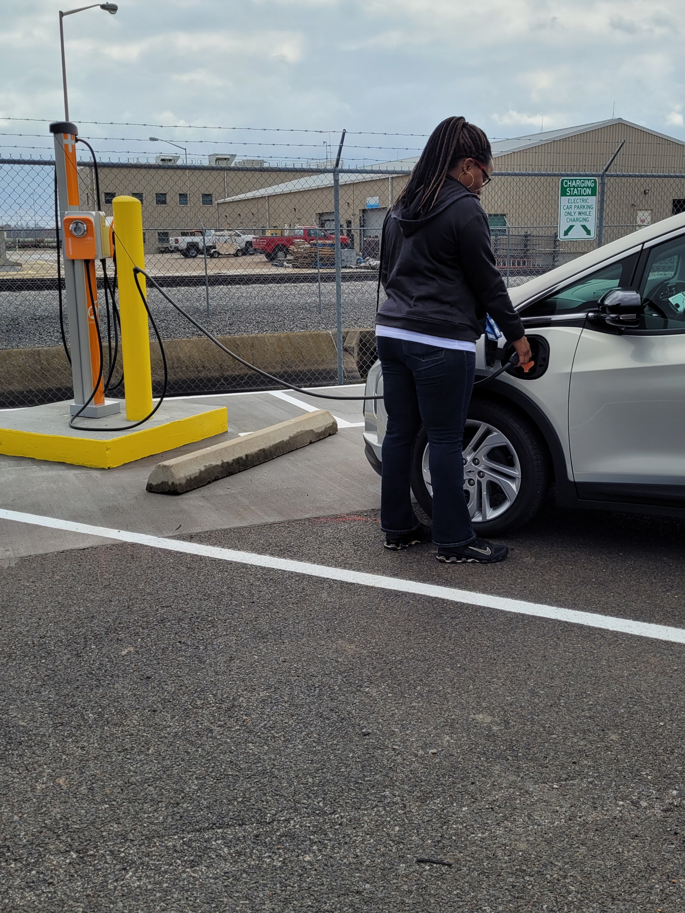 A woman charges a white car using an EV charger