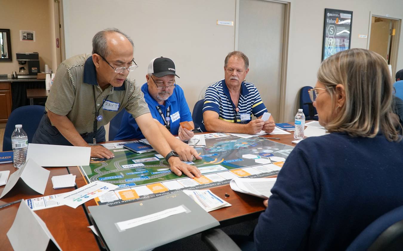 A man explains a laid out paper timeline to a group of people sitting at a table