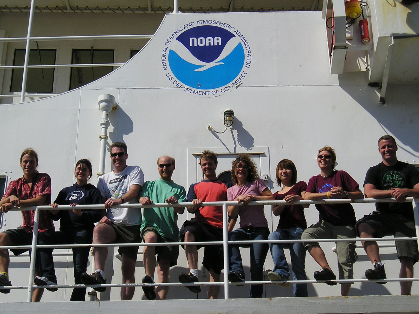 A group of people stand behind a ship's railing.