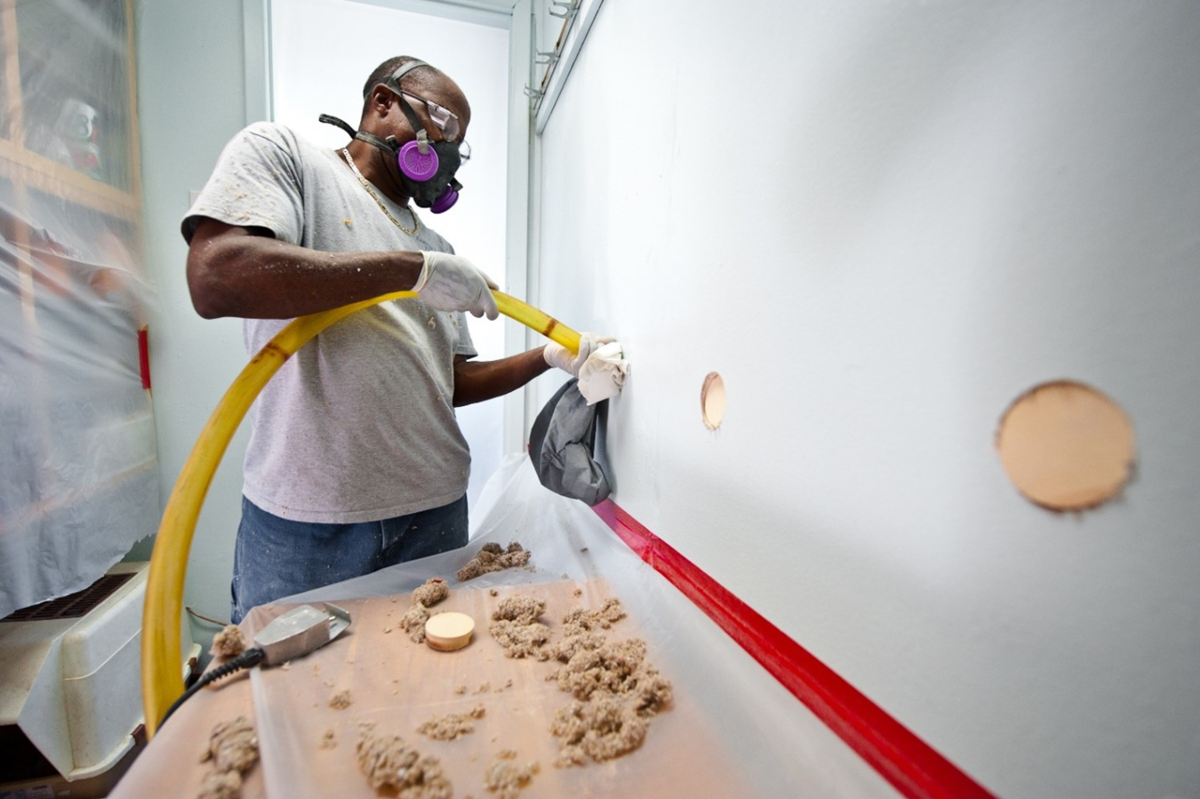 Man wearing a protective mask and working on an interior wall in a building as part of a retrofit project.
