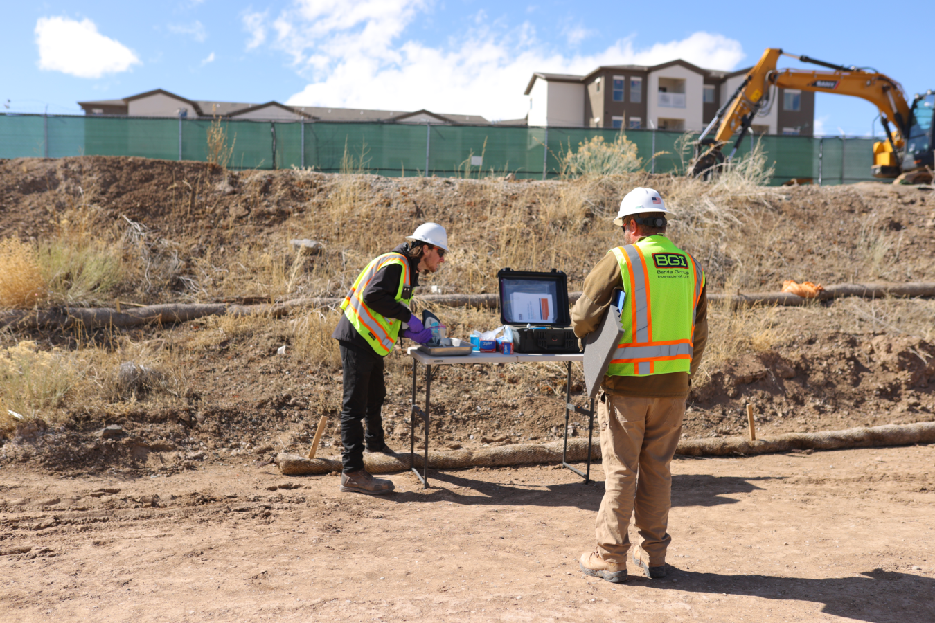 Men stand by a table with a laptop on it in the middle of the field
