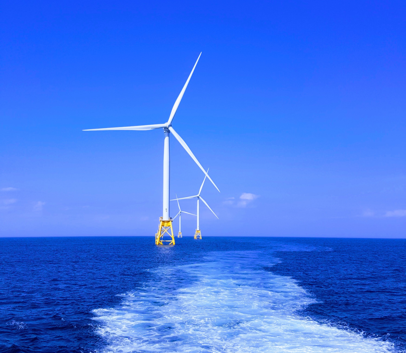 Backwards boat-view of a line of ocean-bound wind turbines.