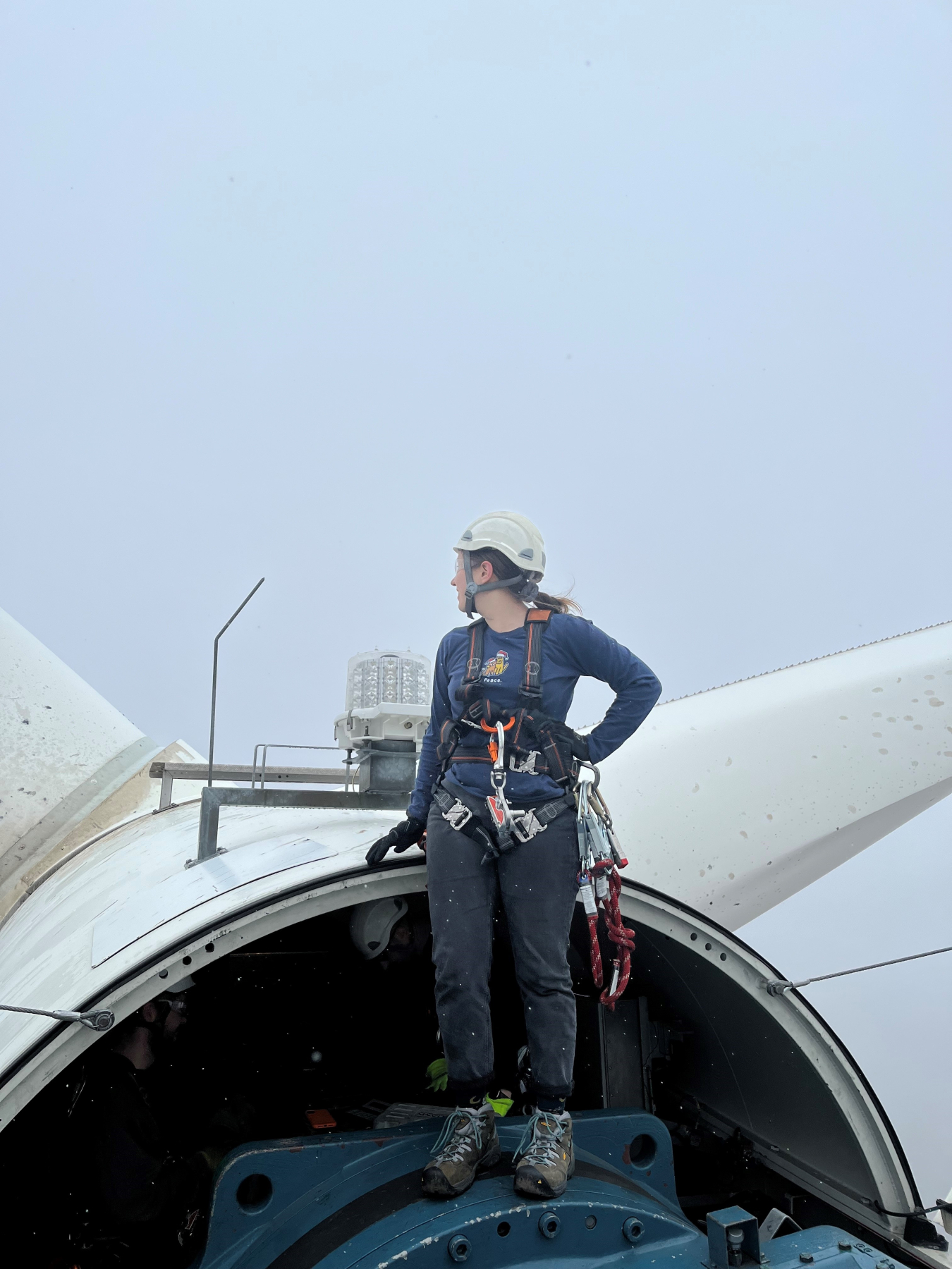 Annika Torp standing on a wind turbine nacelle in a helmet and climbing harness.