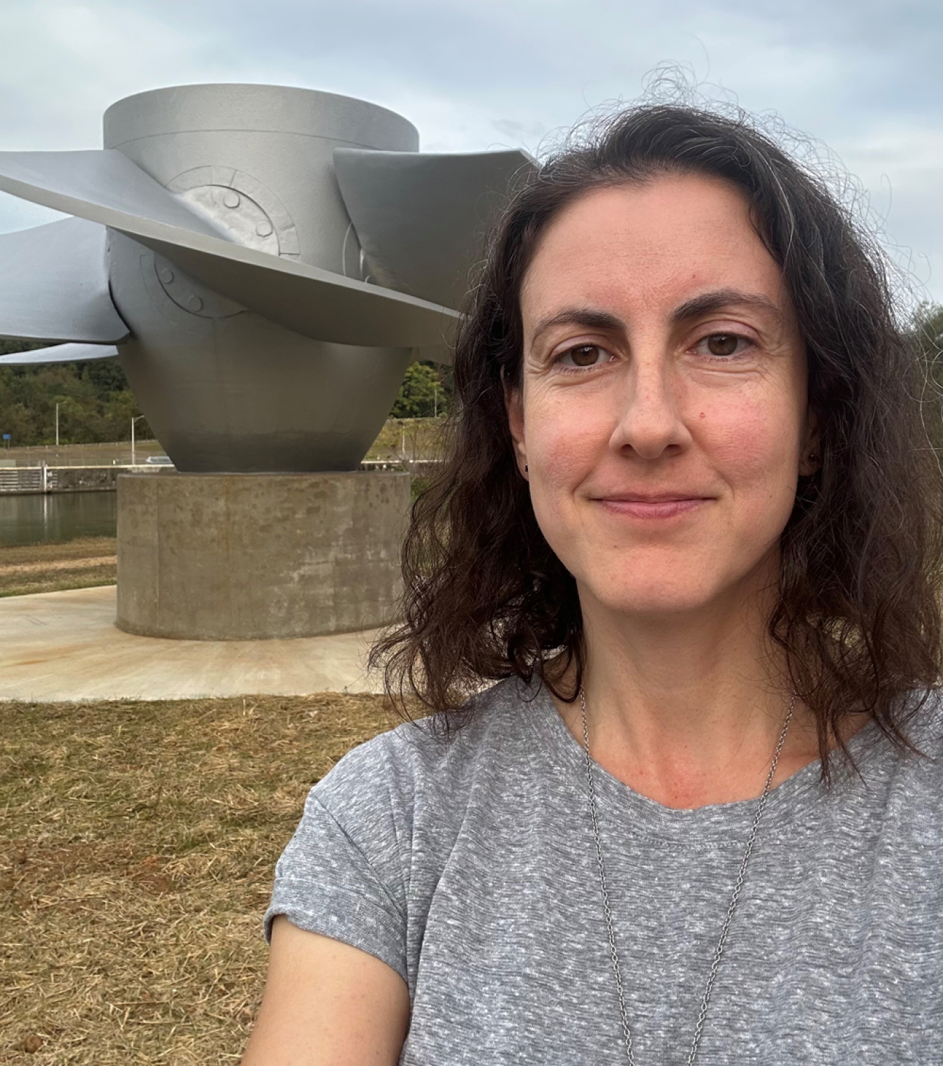 A woman poses in front of a hydropower turbine.