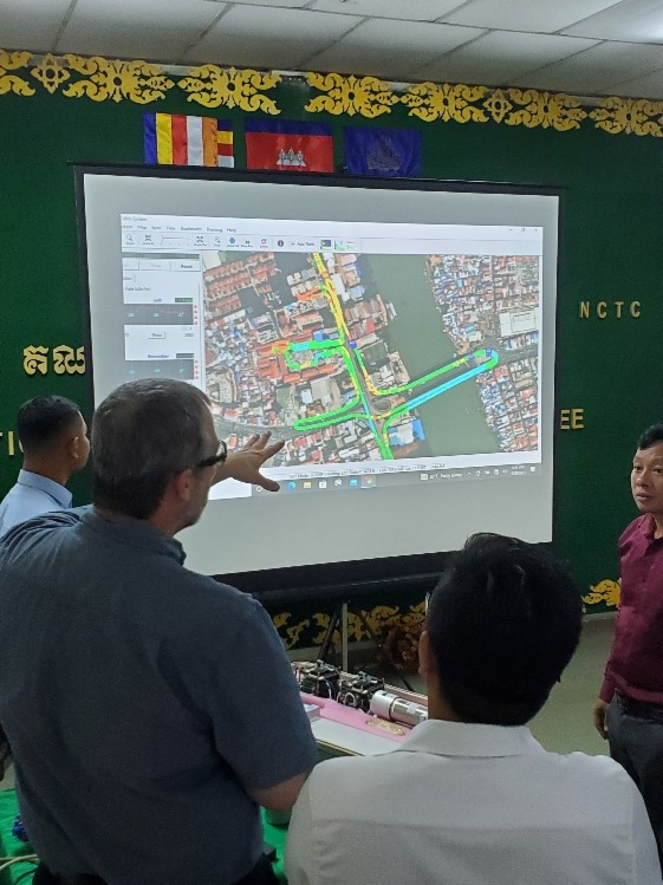 Participants look at a screen showing a satellite image of a city with graphic overlayed.