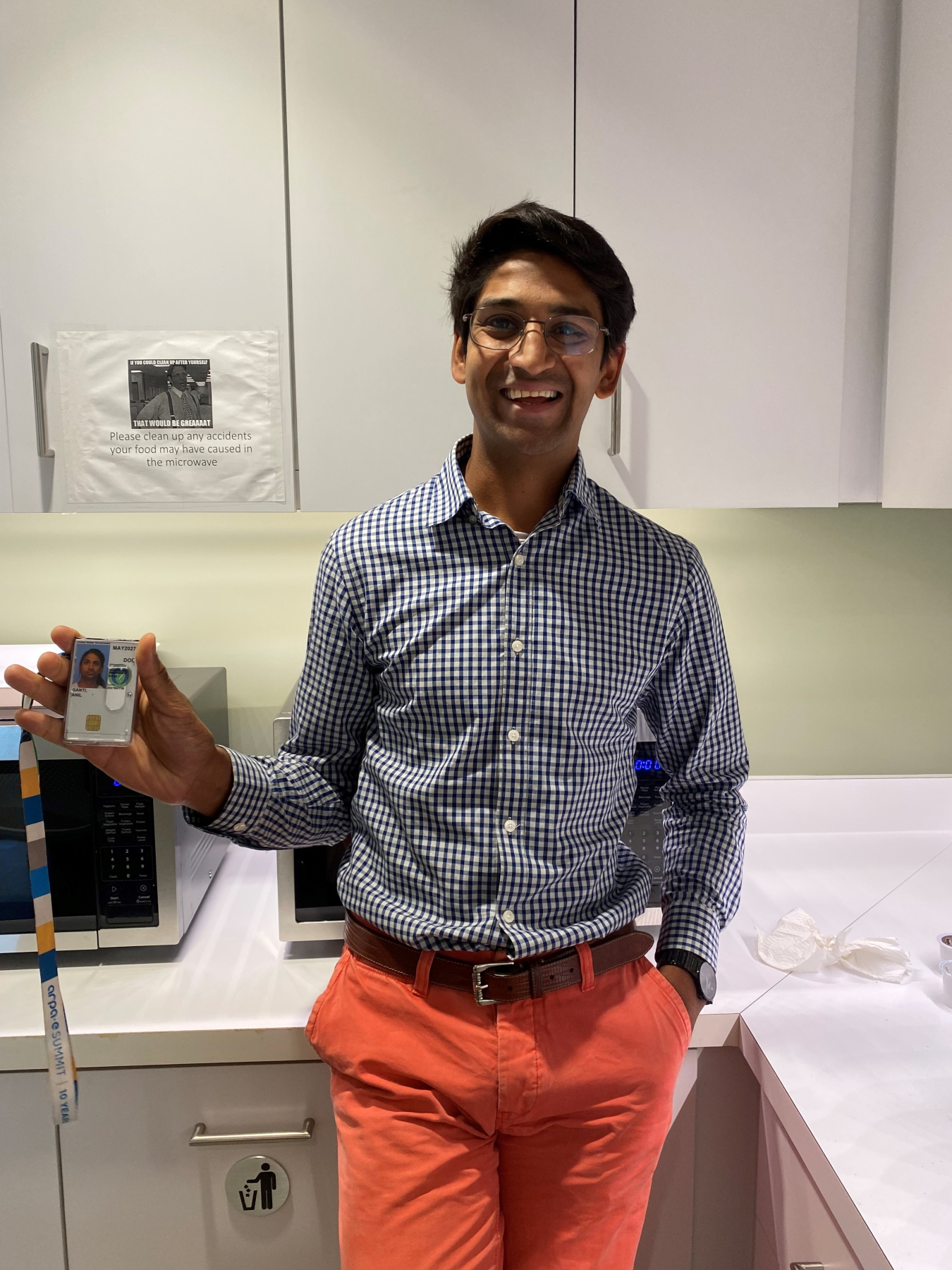 Dr. Anil Ganti stands with one hand in his pocket, holding up a badge with the other hand