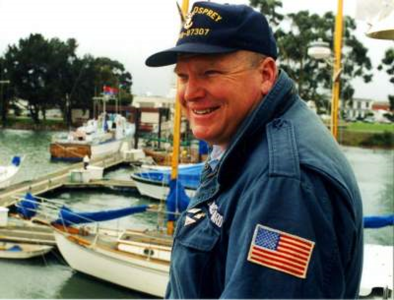 Man with a jacket that has an American flag patch on the sleeve and a hat