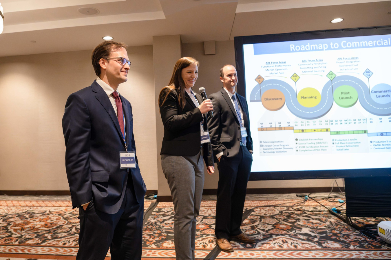 A group of three people professionally dressed, give a PowerPoint presentation in a hotel meeting room.