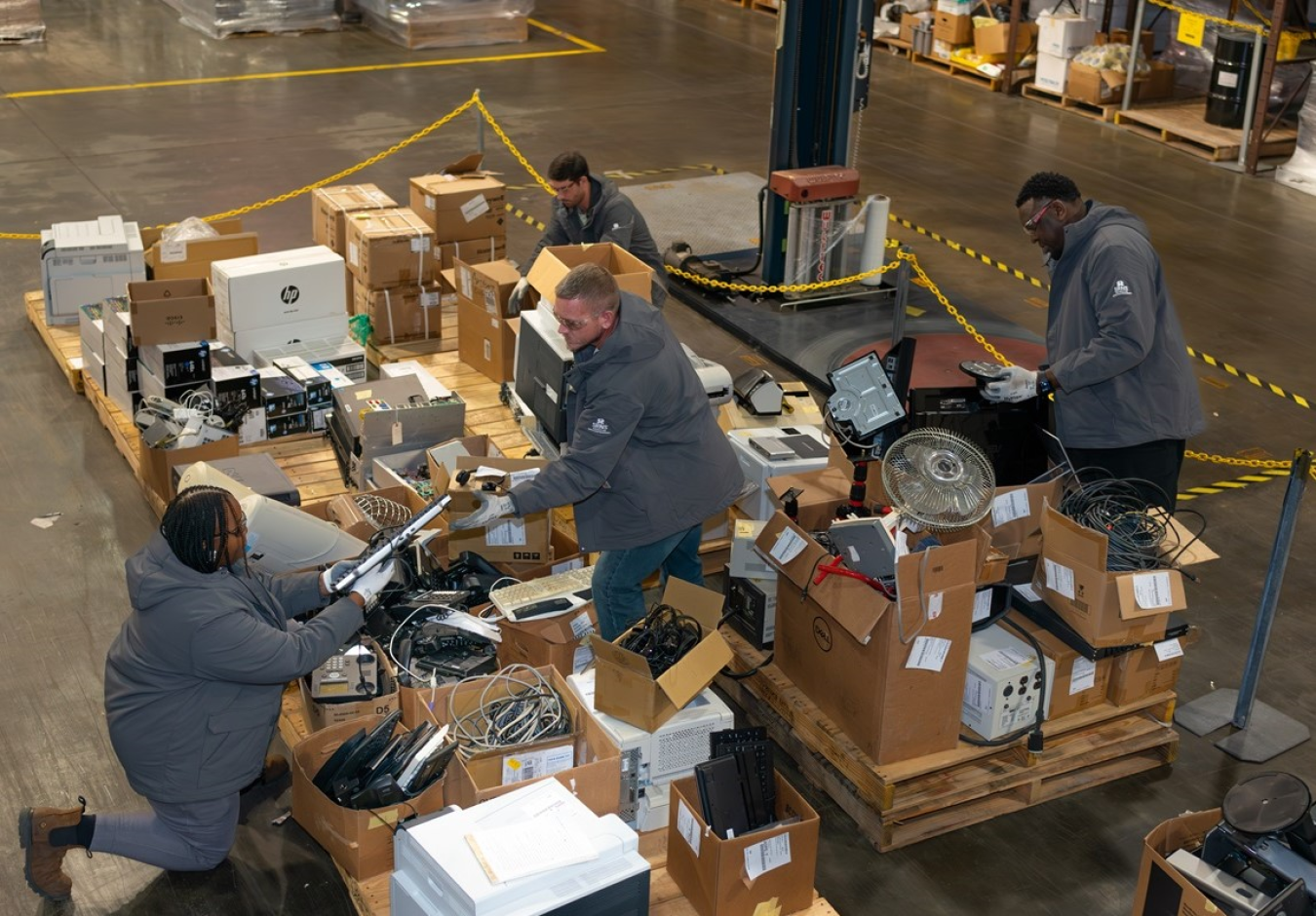 Workers in warehouse load electronics onto wooden pallets