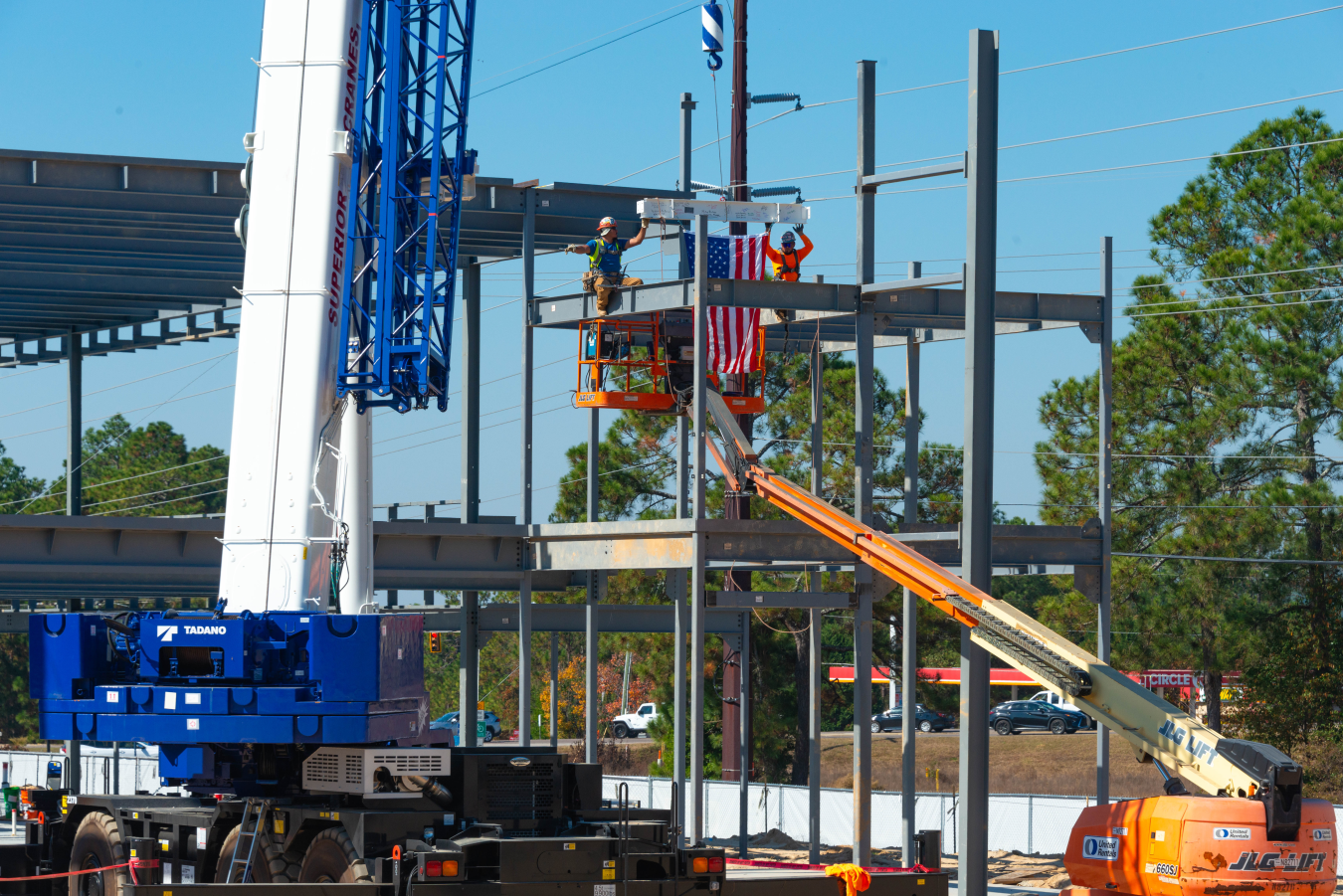 Crews on a crane with a US flag elevated to place the last steel piece to the steel structure.