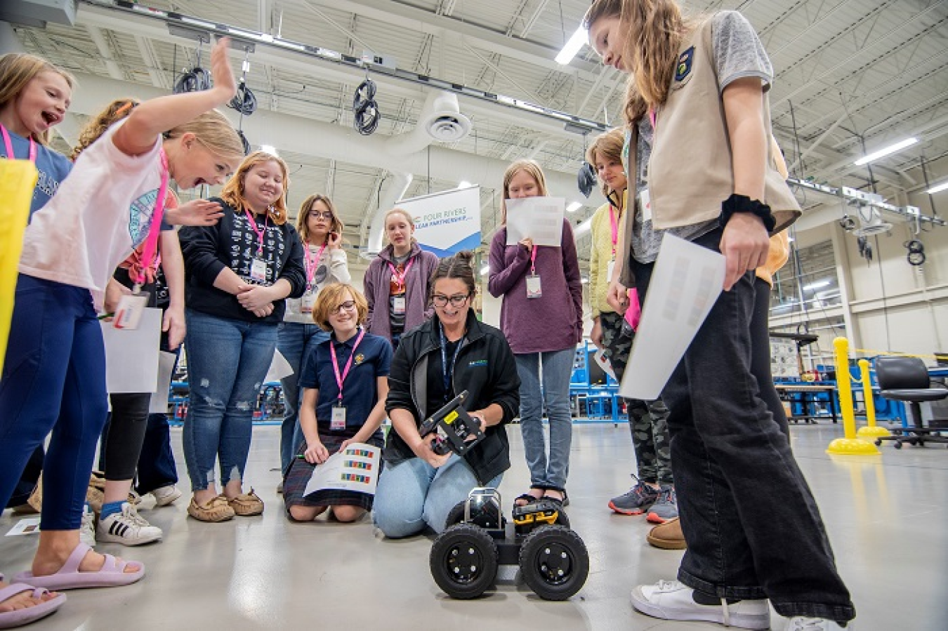 Young girls stand around a woman controlling a robot