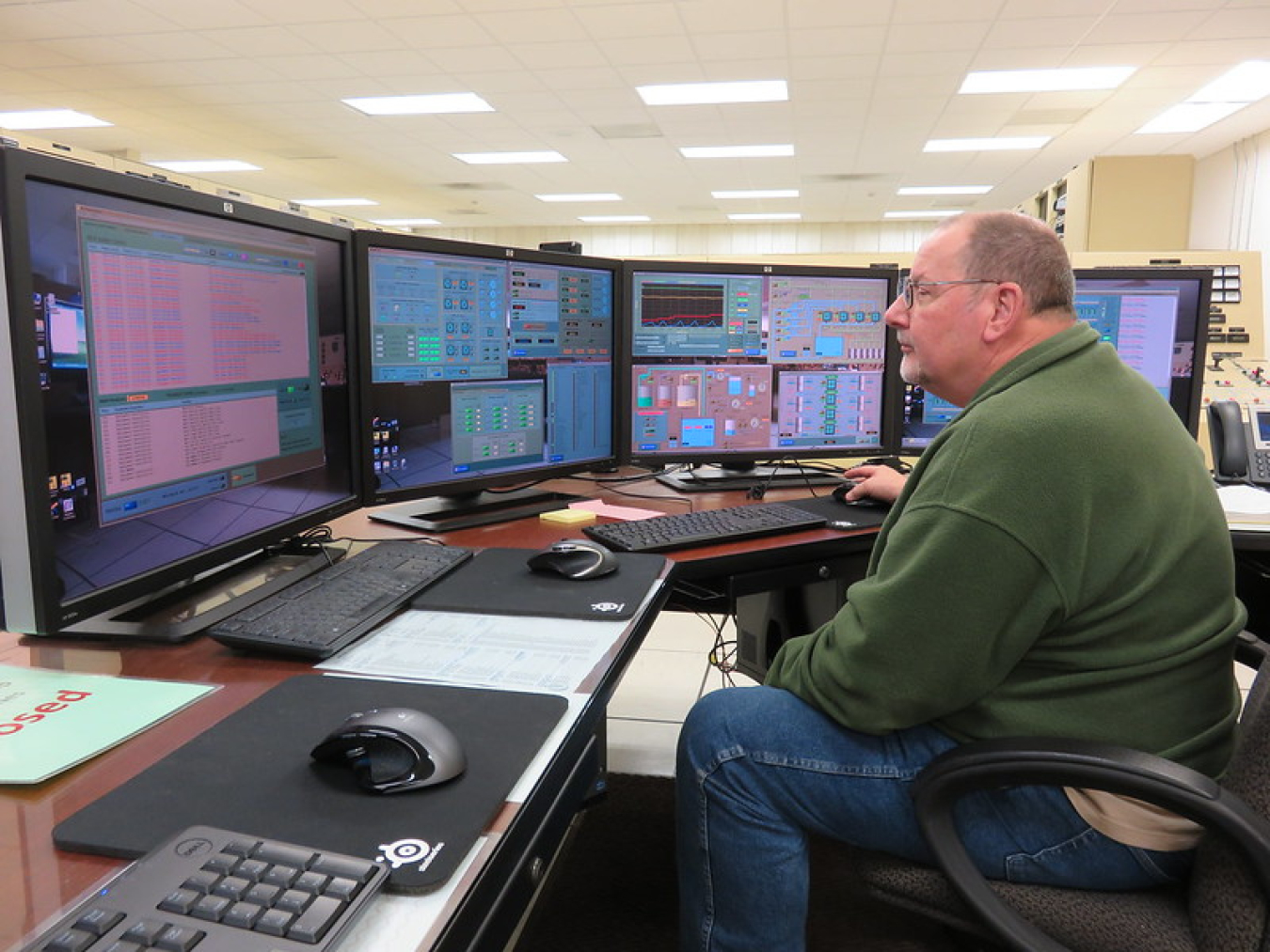 An employee sits looking at computer monitors. 