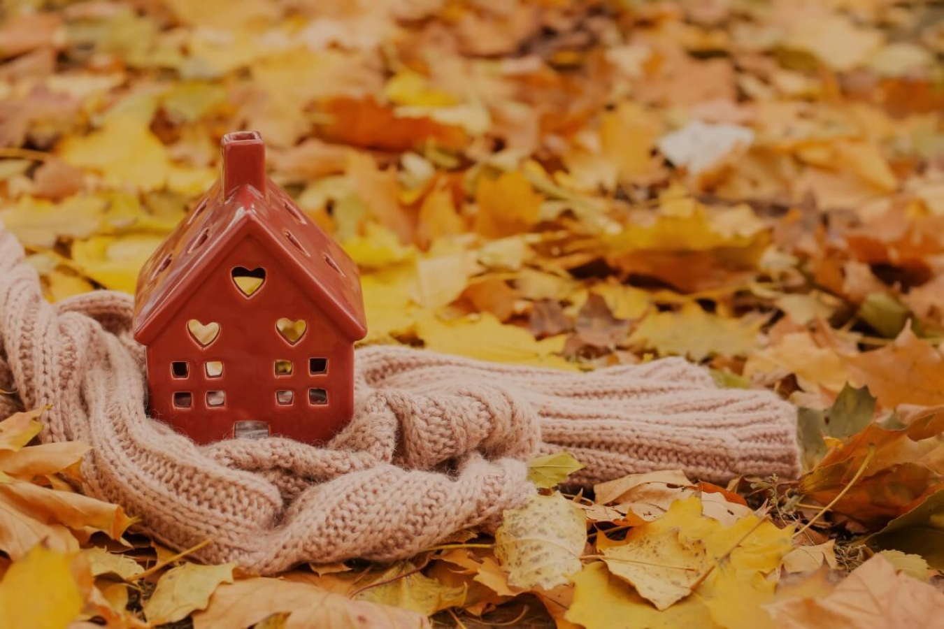 Sweater wrapped around a decorative ceramic house, sitting in autumn leaves on the ground.