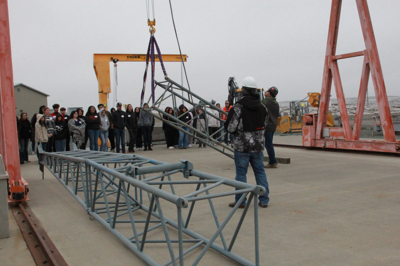 Metal frames getting lifted into the air via machine while students and instructors watch