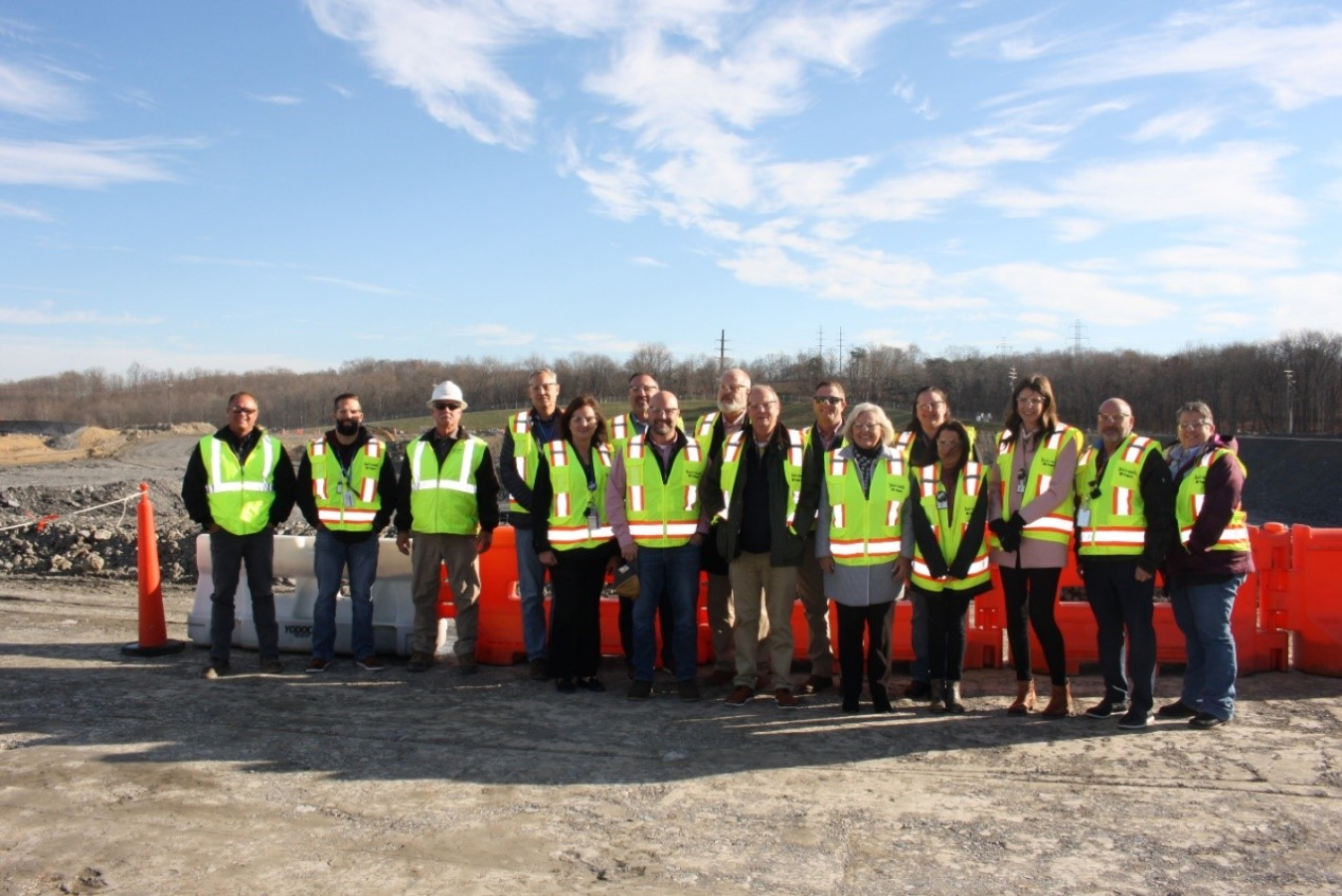 A large group of people pose for a picture standing in a field site wearing neon yellow safety vests