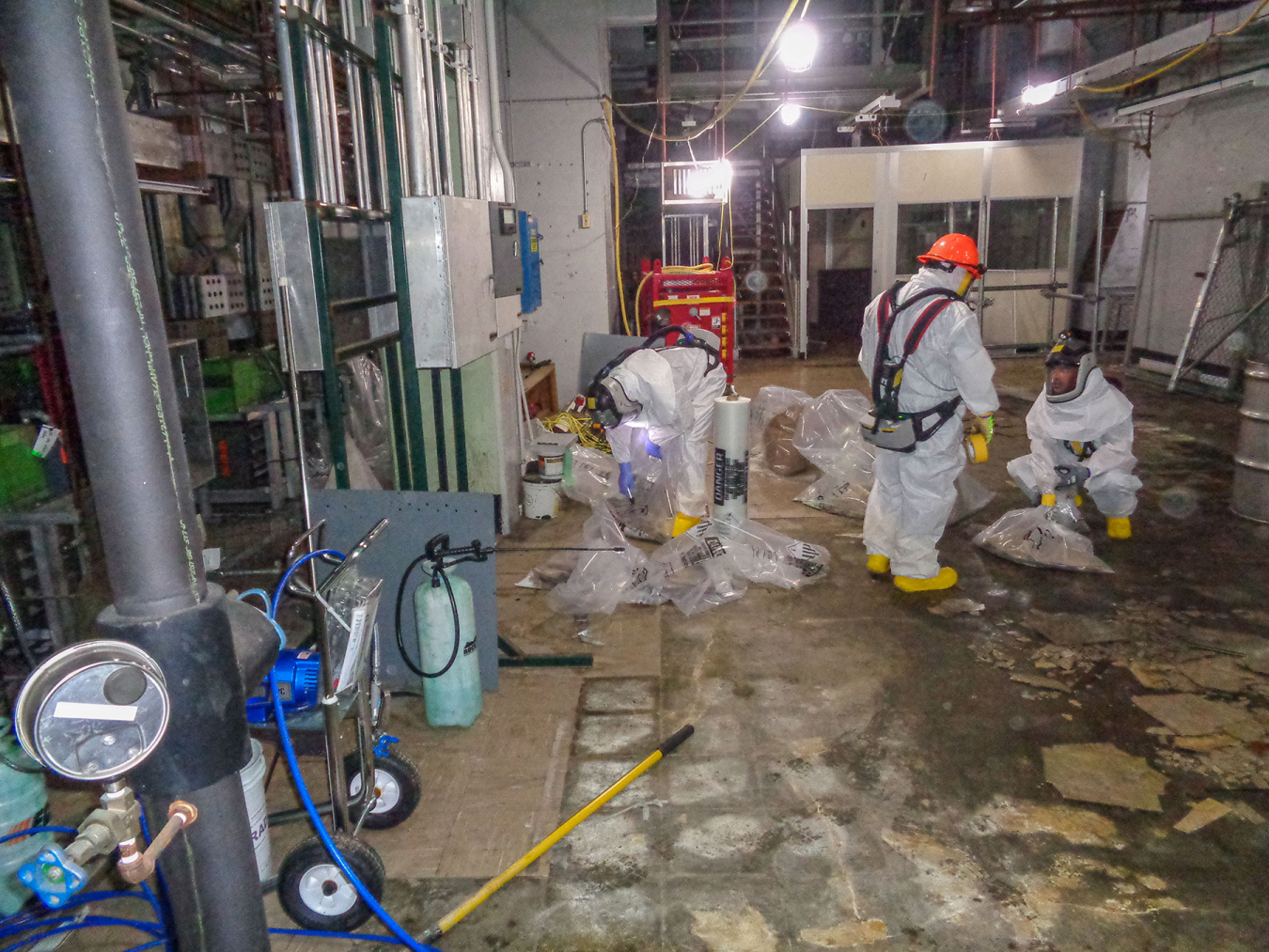 Workers in hazmat suits work to remove asbestos from a large facility room