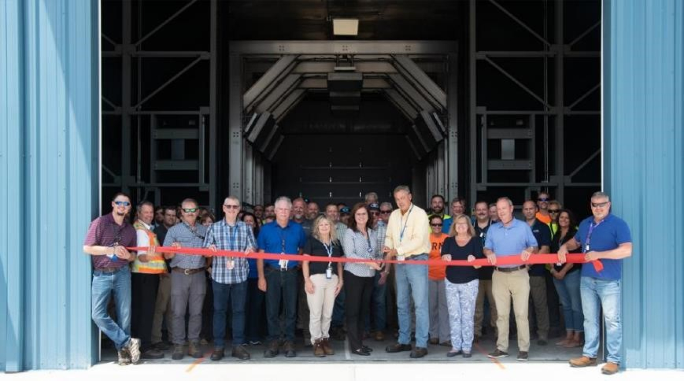 A large group of people pose for a picture while performing a ribbon cutting