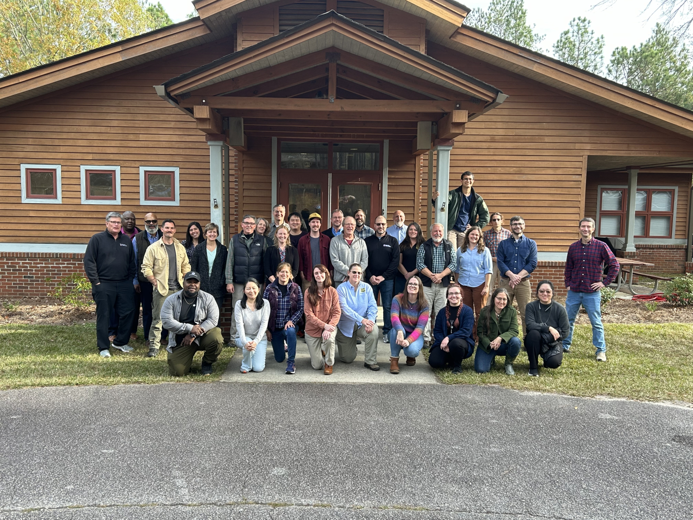 A large group of people pose for a photo in front of a brown building