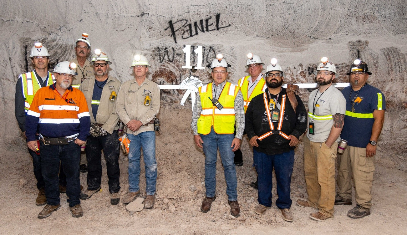 A group of workers in white hard hats pose for a group picture in WIPP's underground disposal facility