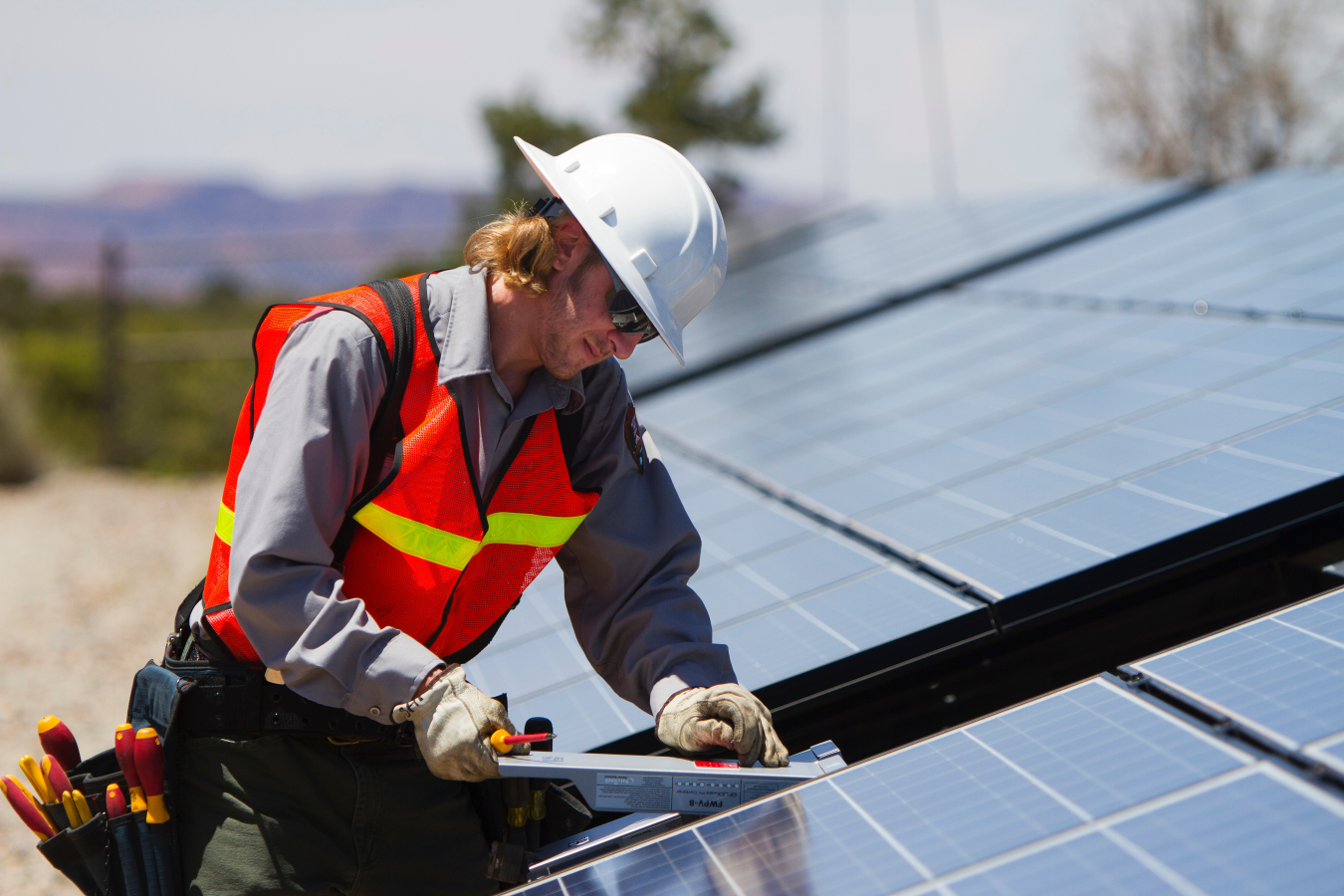 Photo of a man in an orange vest and hard hat performing maintenance on a PV array.