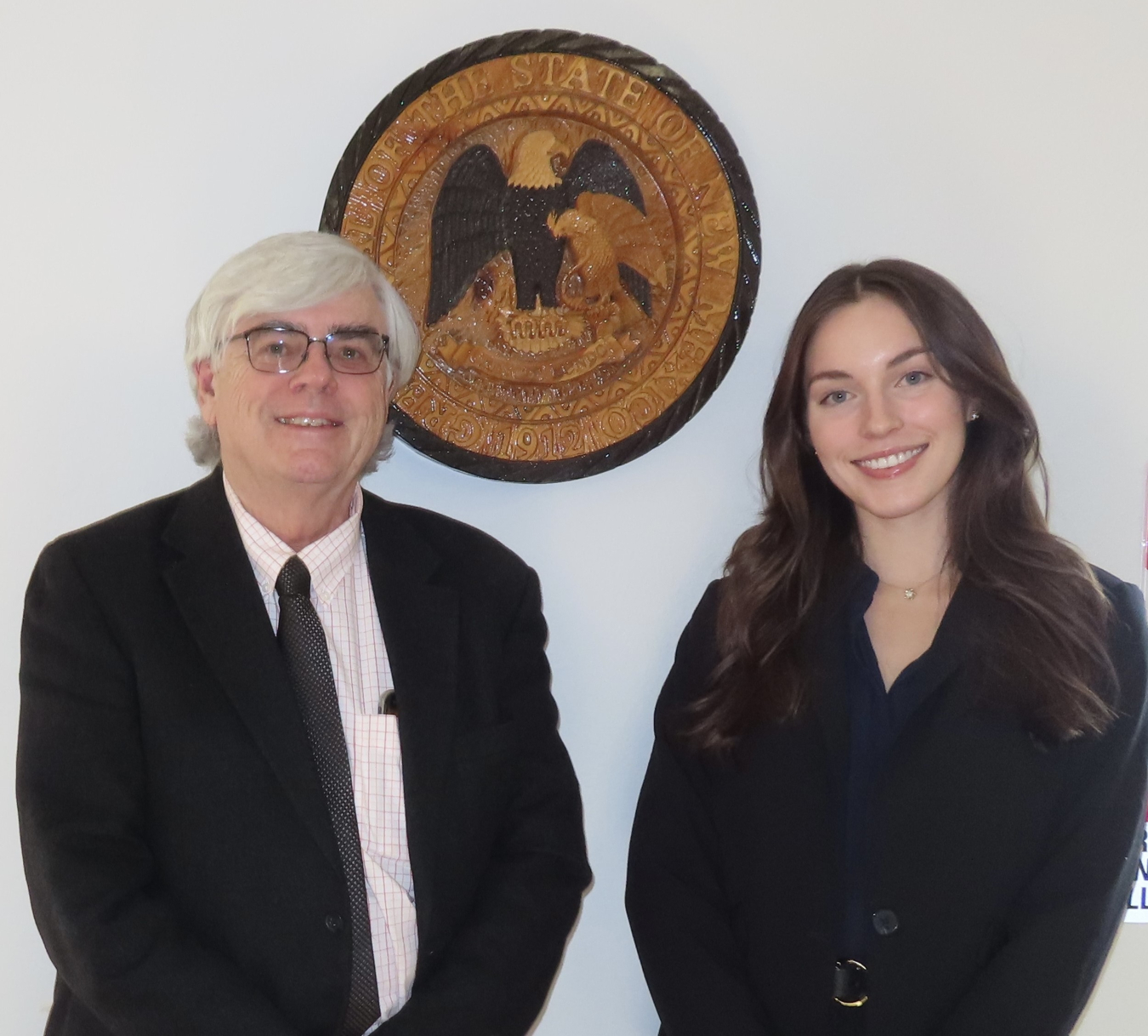 CEIF mentor Arthur O’Donnell standing next to Fellow, Meredith Tidwell in front of a New Mexico State Seal on the wall.
