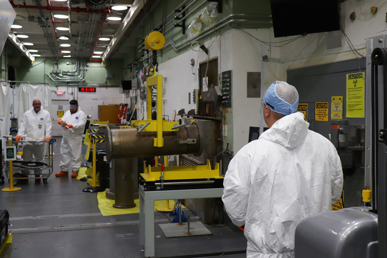 Employees in while protective uniforms loading a canister