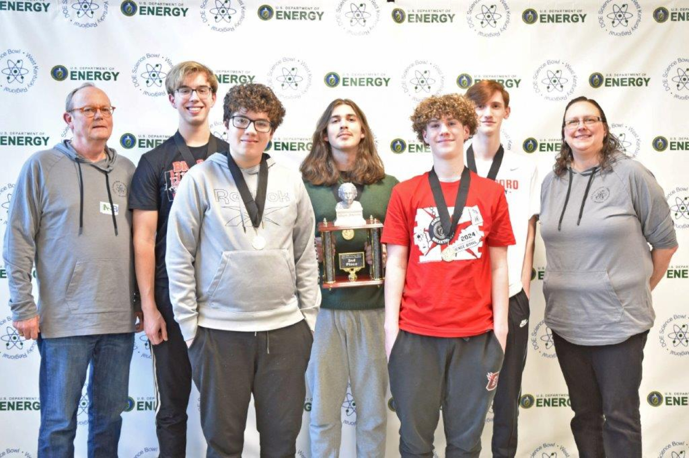 A group of high school students wearing medals pose for a picture with a trophy