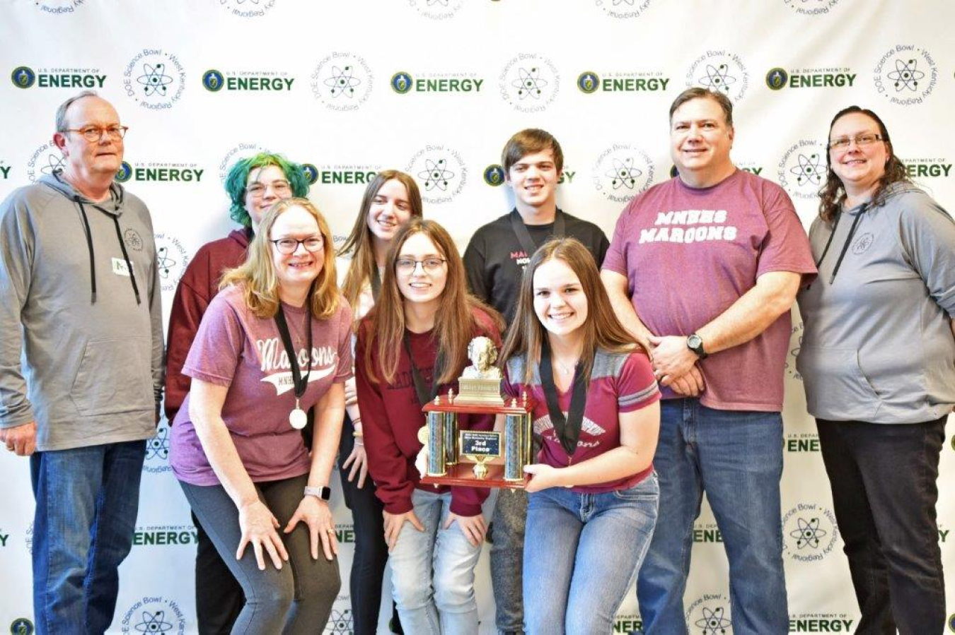 A group of high school students pose for a picture with a trophy while wearing medals