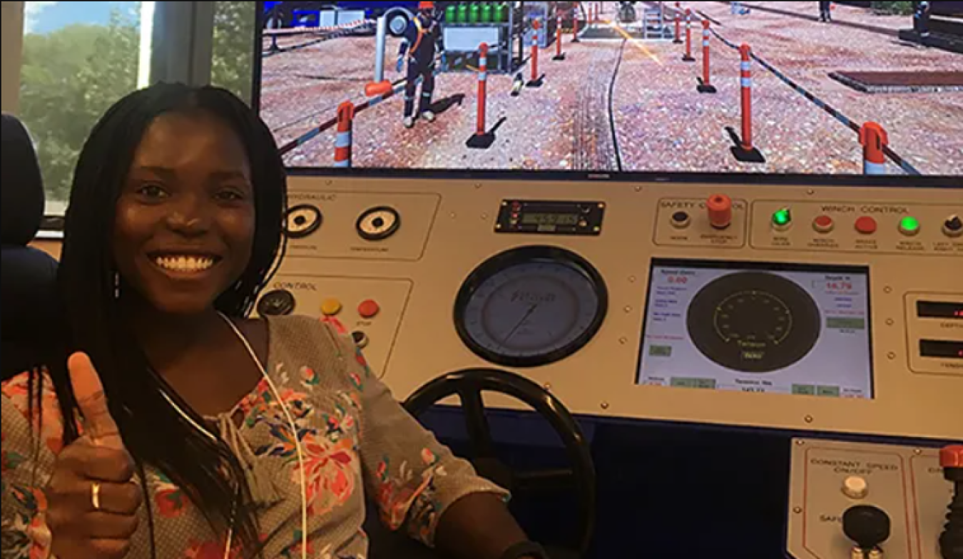 Seyi Sholanke sitting at a driving simulator giving a thumbs up