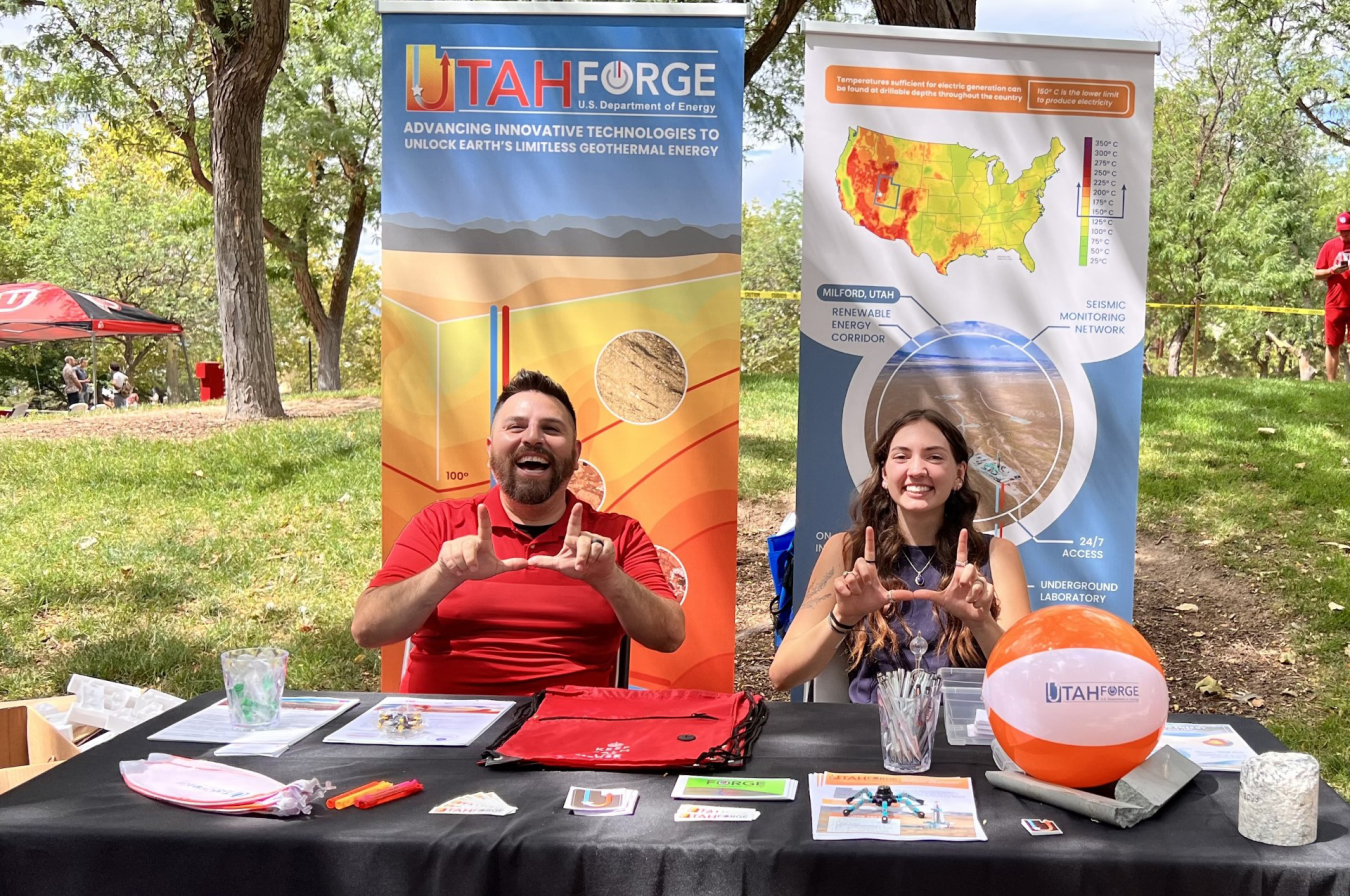 University of Utah students BJ Iturrieta and Sarah Buening sit at the Utah FORGE booth with smiles on their faces, making a U with their hands (called 'flashing the U' at University of Utah) during the university's Welcome Week.