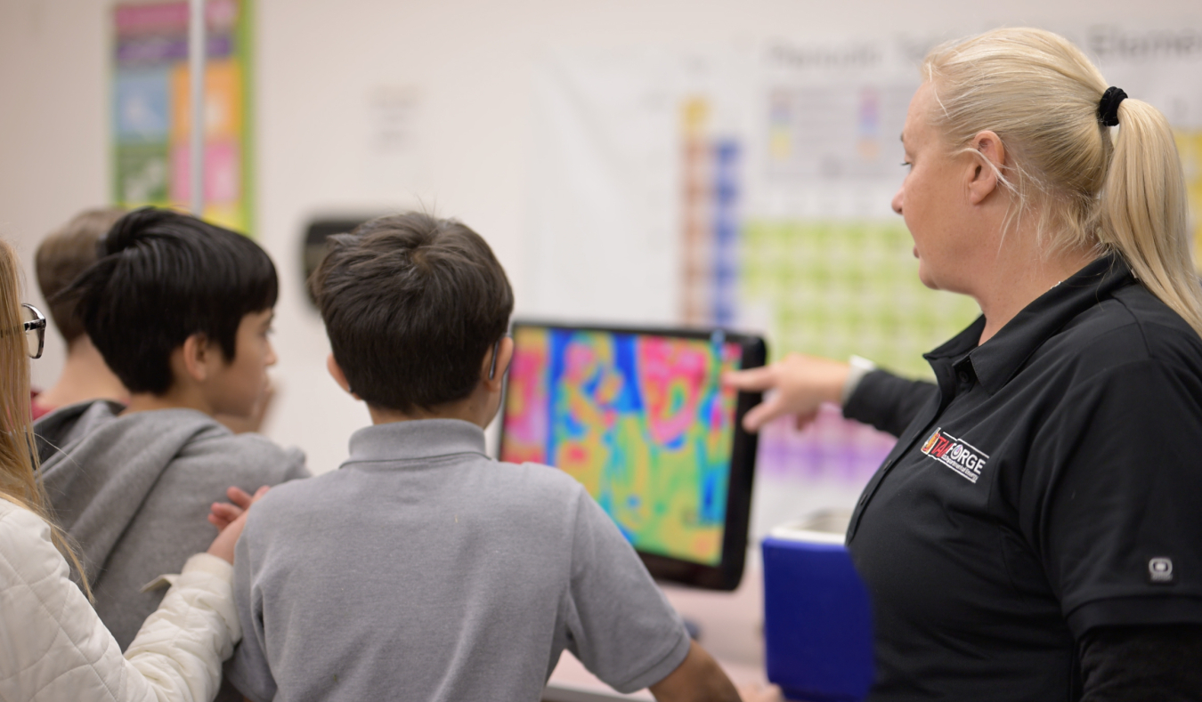 Utah FORGE's Gosia Skowron points at computer screen displaying heat imaging as she discusses thermal characteristics while four students look on in a classroom visit.