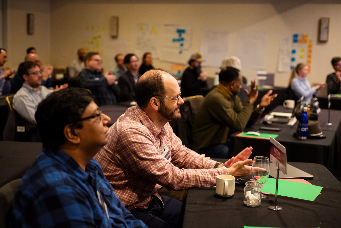 A group of people sitting at tables in a meeting room listening to a presentation.