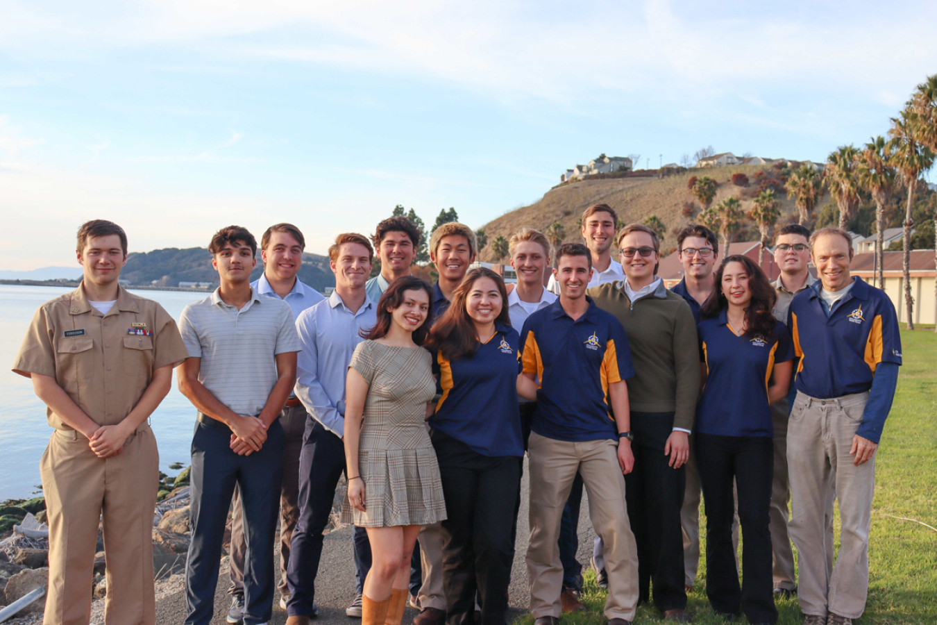 A group of people standing on a cliff next to the ocean. 