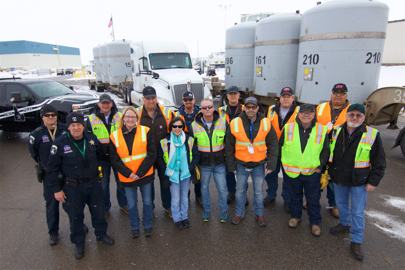 Group photo of workers in front of vehicles and large grey tanks