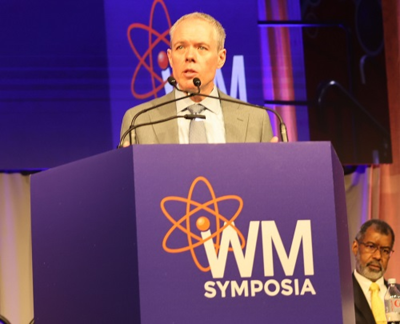 A man standing at a podium speaking on stage at a conference