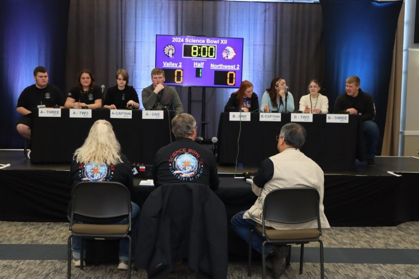 A group of students participating in a science bowl sitting on stage answering questions