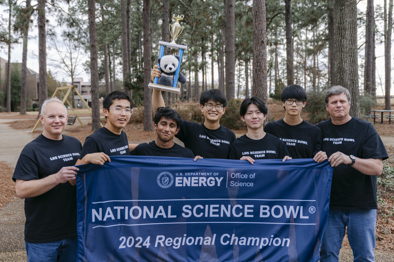 A group of high school students and their coaches hold up a winners banner