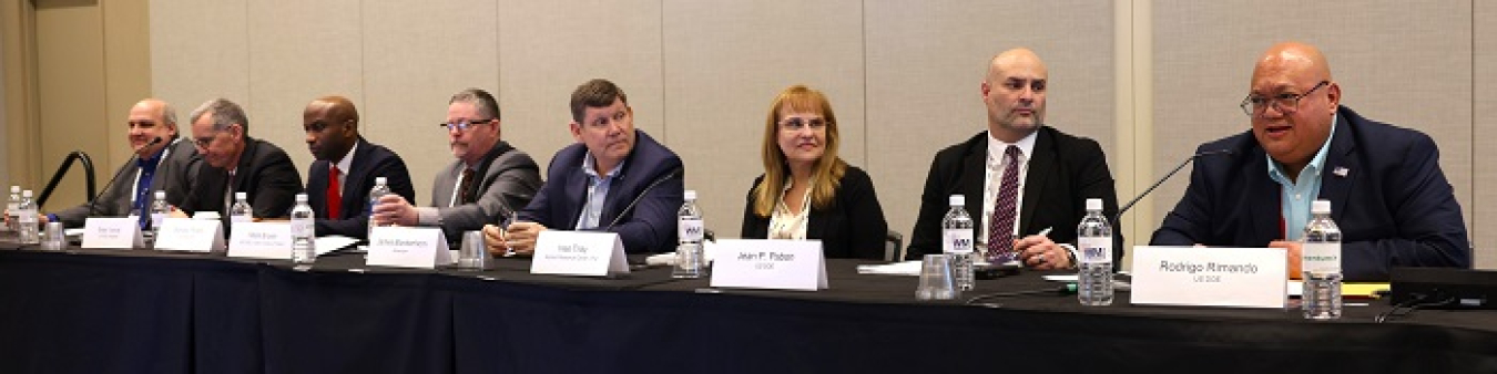 A group of panelists sitting at a table on a stage speaking into microphones