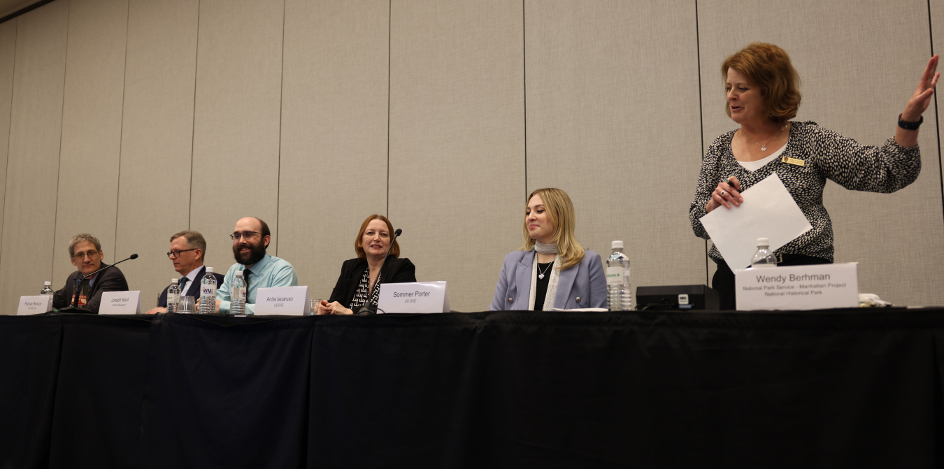 A group of panelists sitting at a table on a stage speaking into microphones