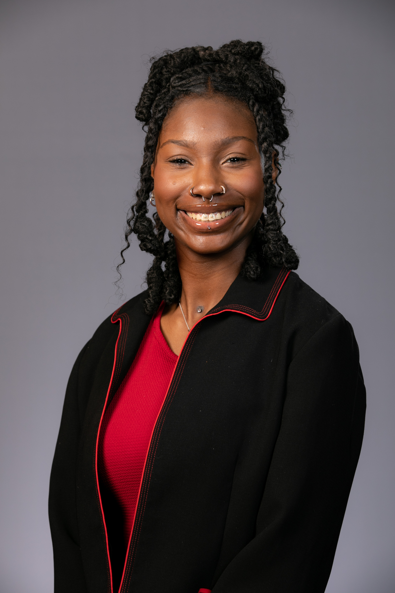 Professional headshot of a young woman in a red shirt and black blazer