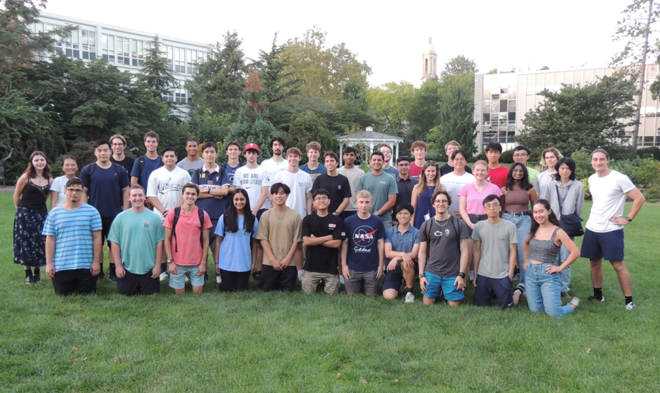 A large group of people standing and kneeling in rows on a grassy field. 