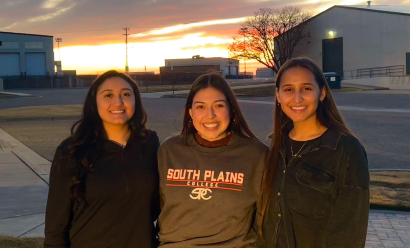 Three students standing in front of a sunset