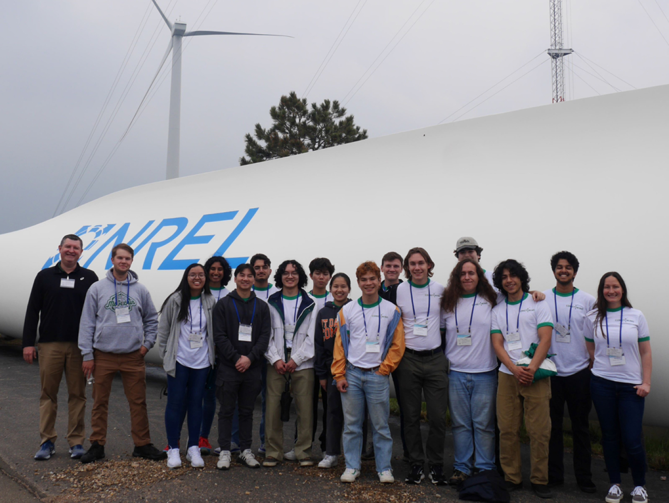 A group of people standing in front of a wind turbine blade laying on the ground.