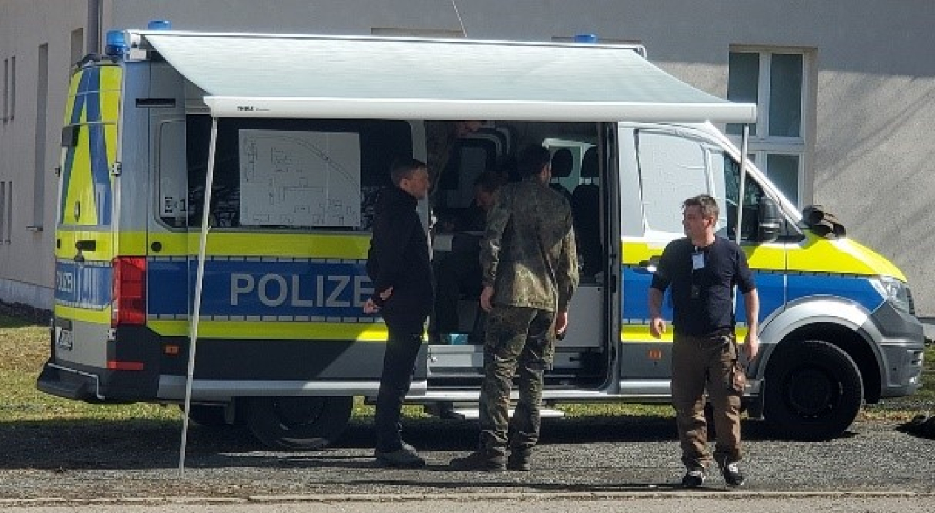 A group of three German police stand next to a police van.