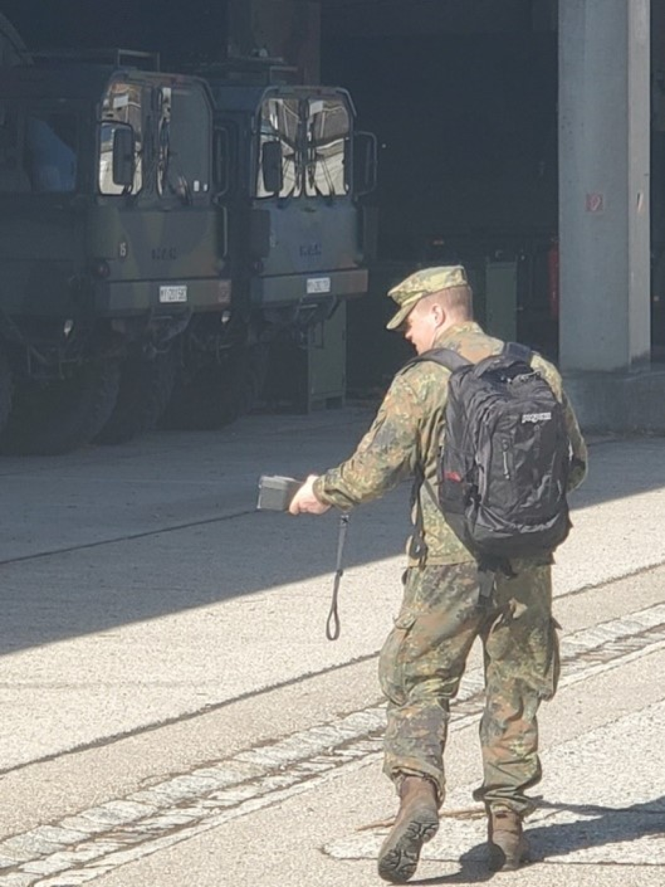 A man dressed in military fatigues shown from the back takes a reading from a handheld radiation monitor.